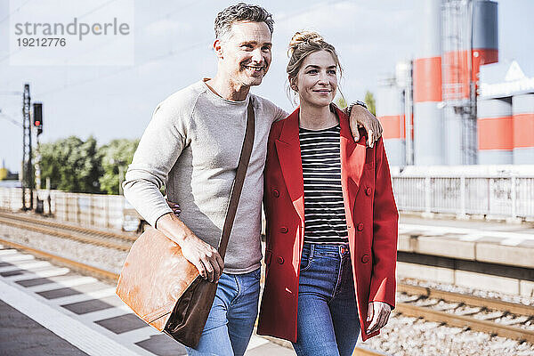 Lächelnder Mann und Frau  die an einem sonnigen Tag gemeinsam am Bahnsteig spazieren