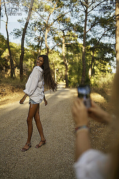Frau fotografiert Tochter im Teenageralter  die auf der Straße im Wald steht