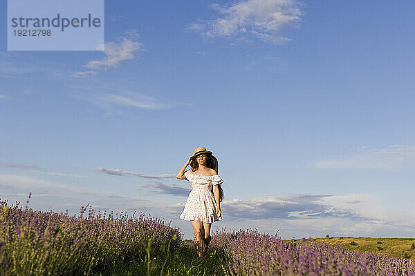 Frau im weißen Kleid spaziert an einem sonnigen Tag auf dem Feld