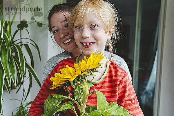 Teenage girl with blond sister holding sunflower on balcony