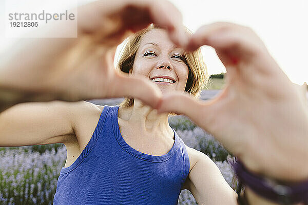 Smiling woman gesturing heart shape in lavender field