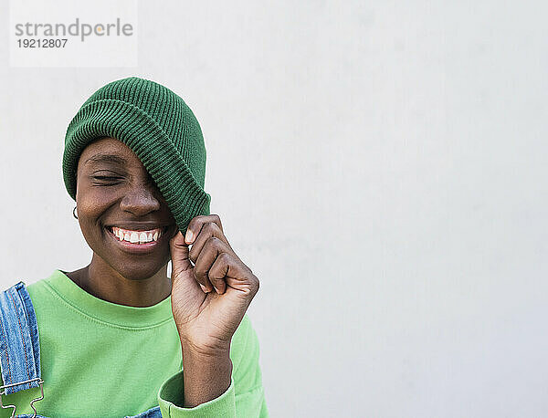 Happy woman holding green knit hat in front of white wall