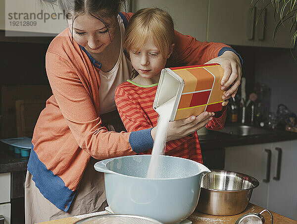 Teenage girl helping sister to pour sugar in bowl at home