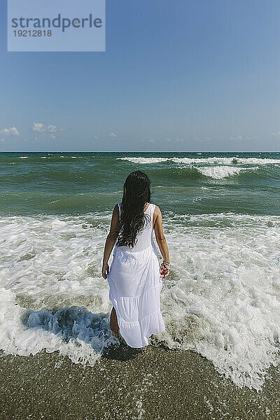 Frau blickt aufs Meer und steht am Strand