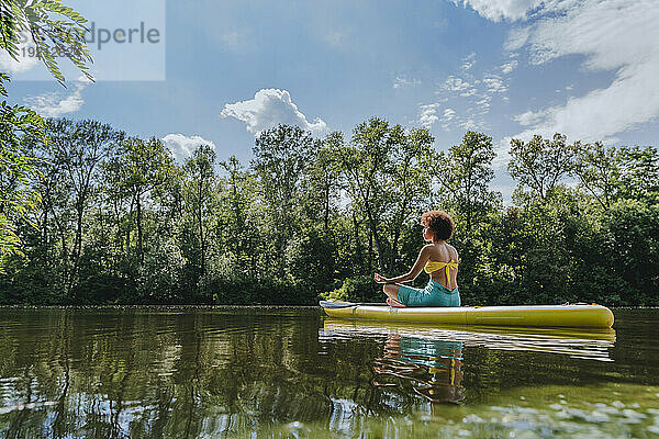 Junge Frau meditiert auf einem Paddleboard im See