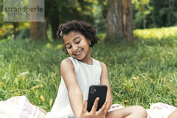 Lächelndes Mädchen macht Selfie mit Smartphone im Garten