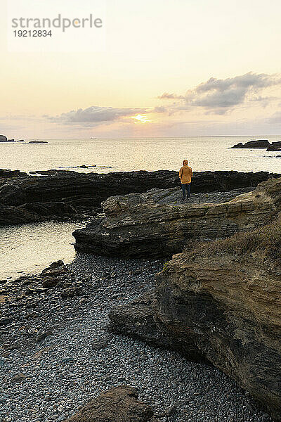 Frau steht auf einem Felsen am Strand unter freiem Himmel