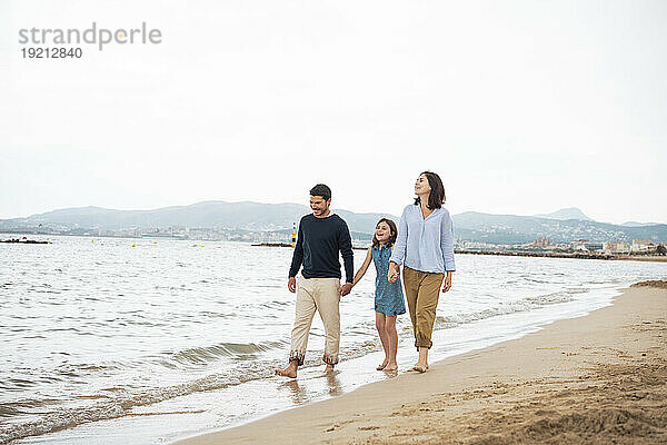 Glückliches Mädchen  das mit Vater und Mutter am Strand spaziert