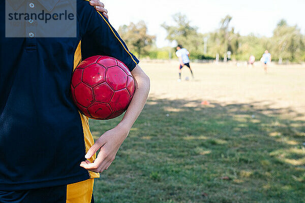 Mädchen hält roten Fußball auf dem Sportplatz