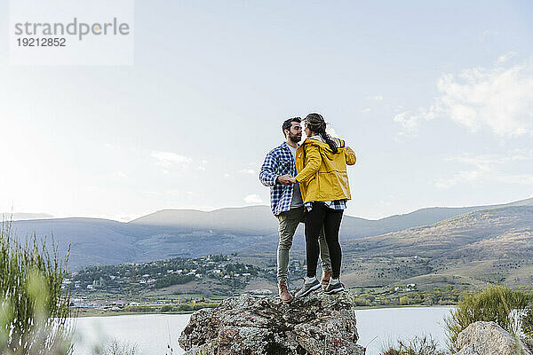 Affectionate couple standing together on rock in front of mountain