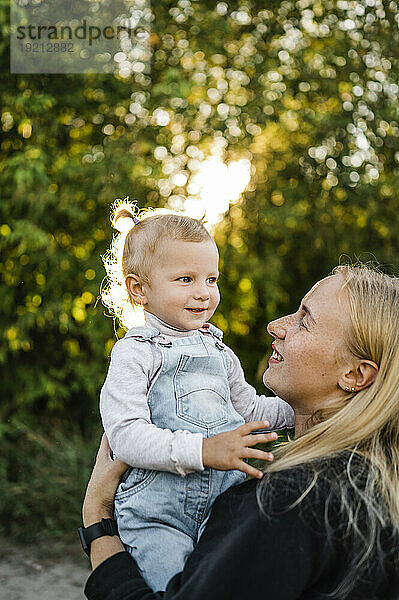 Lächelnde blonde Frau trägt Tochter im Park