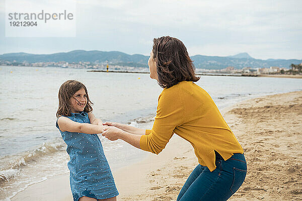 Fröhliches Mädchen hält Händchen und hat Spaß mit der Mutter am Strand