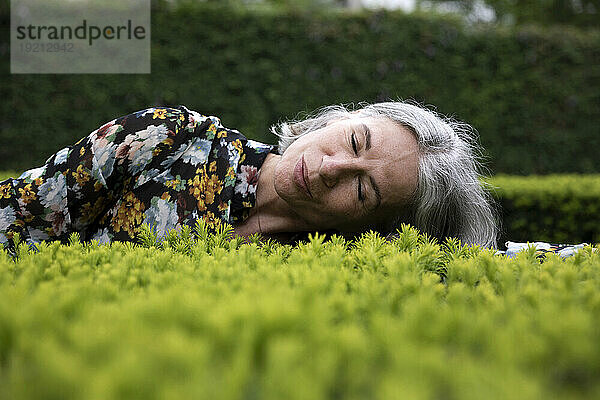 Ältere Frau liegt auf Pflanzen im Park
