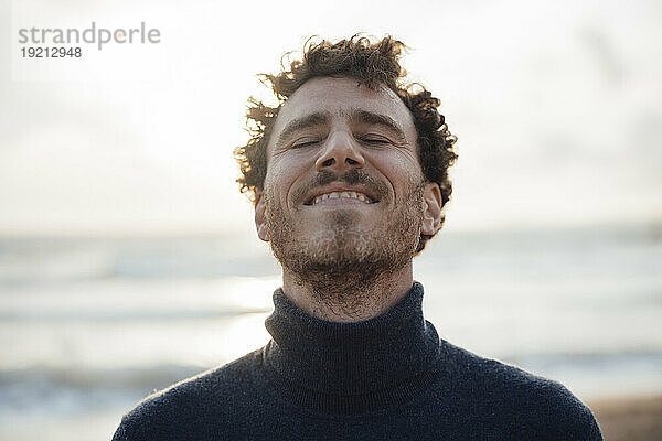 Lächelnder Mann mit geschlossenen Augen am Strand