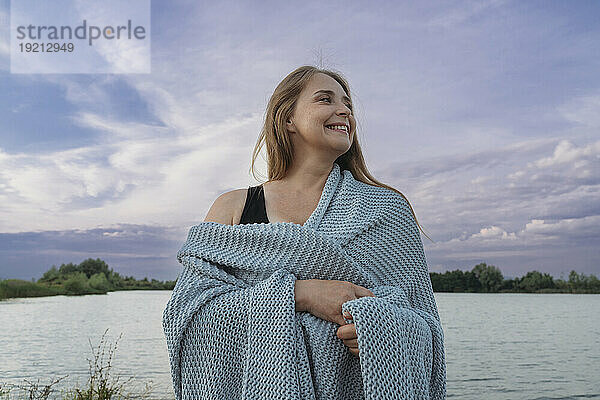 Lächelnde Frau  in Wollschal gehüllt  steht am See