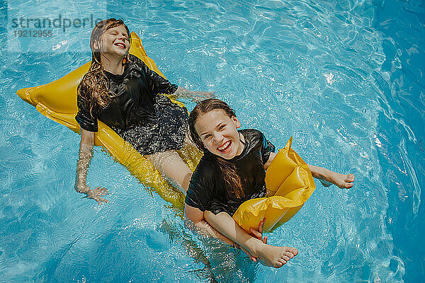 Fröhliches Mädchen  das an einem sonnigen Tag mit einer Freundin auf dem Poolfloß genießt