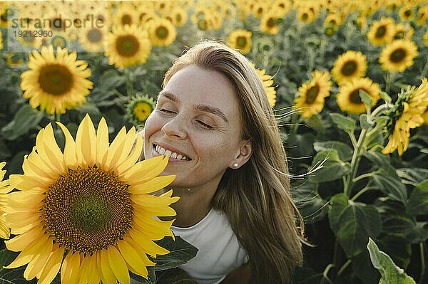 Lächelnde Frau mit geschlossenen Augen neben Sonnenblume im Feld