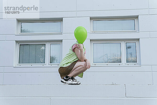 Frau mit Luftballon kauert vor Gebäude