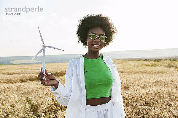 Glückliche Frau mit Brille hält Windkraftanlage im Feld