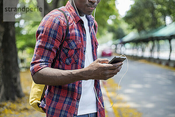 Junger Mann hört Musik und hält sein Smartphone auf der Straße