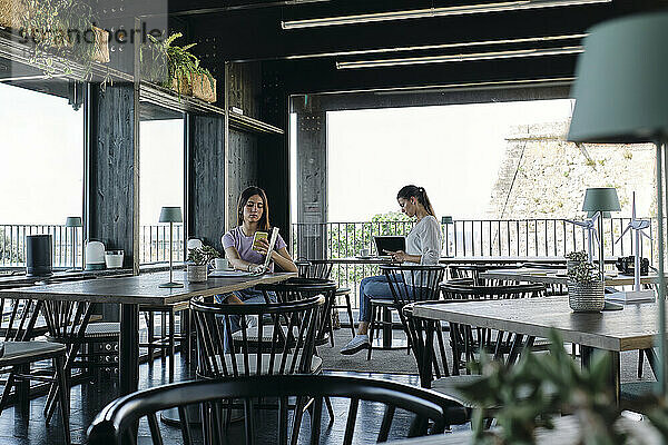 Zwei junge Frauen sitzen mit Smartphones in der Hand an Cafétischen