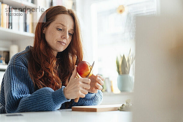 Frau schneidet Apfel mit Messer in der heimischen Küche
