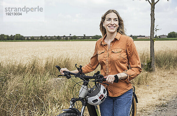 Glückliche Frau  die mit dem Fahrrad in der Nähe des Feldes steht