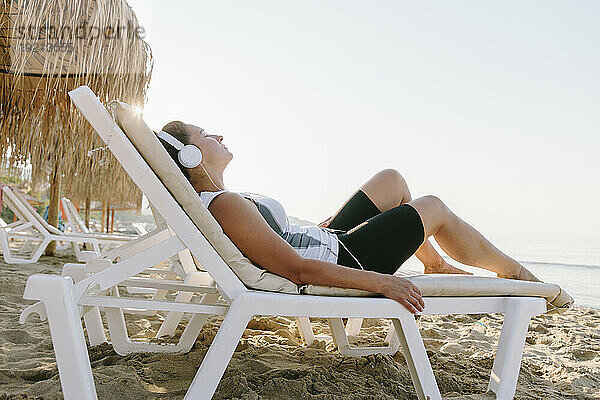 Frau mit Kopfhörern entspannt sich im Liegestuhl am Strand