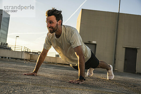 Active man doing push-ups on building terrace at sunset