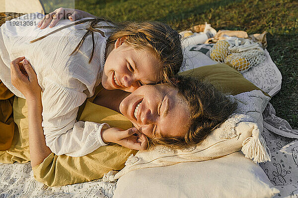 Glückliche Mutter umarmt Tochter bei Sonnenuntergang auf der Picknickdecke