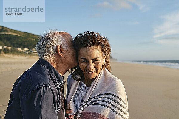 Älterer Mann umarmt glückliche Frau am Strand an einem sonnigen Tag