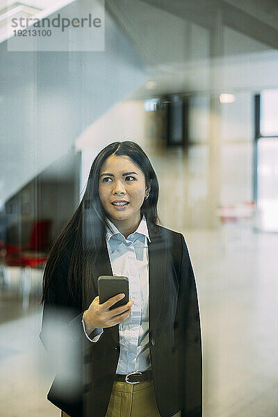 Geschäftsfrau mit Smartphone am Arbeitsplatz durch Glas gesehen
