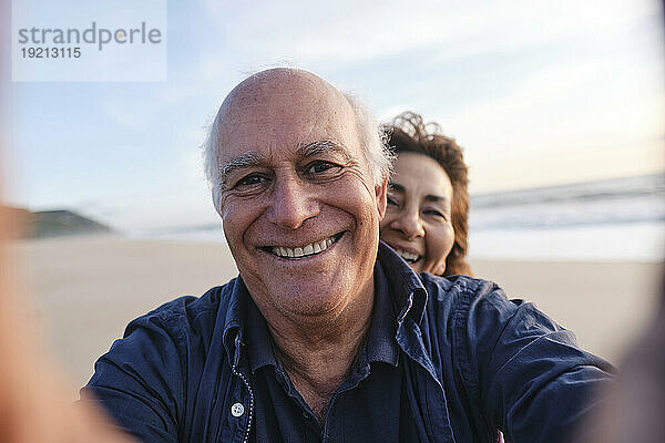 Glücklicher älterer Mann  der am Strand ein Selfie mit einer Frau macht