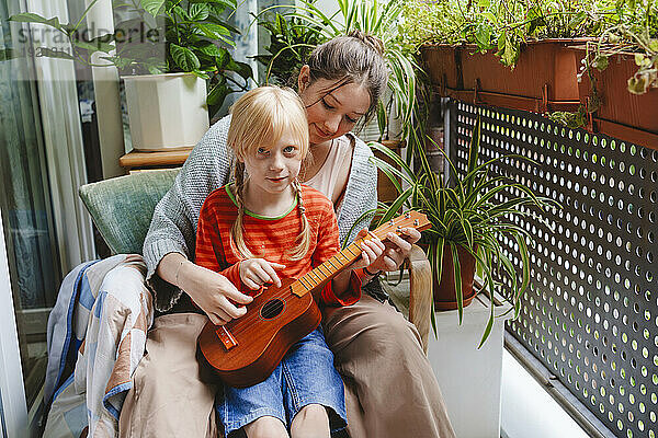 Teenage girl teaching sister how to play ukulele on balcony