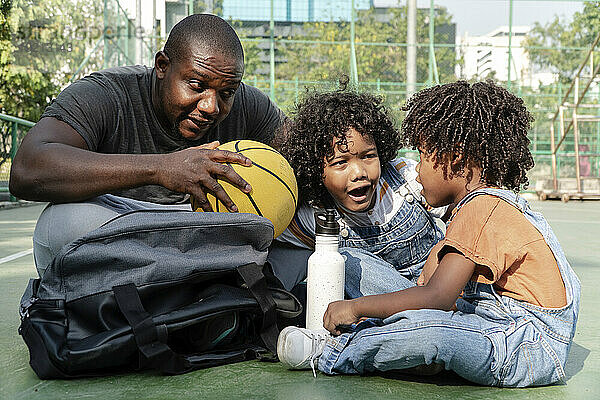 Vater mit Söhnen sitzt und redet auf dem Basketballplatz