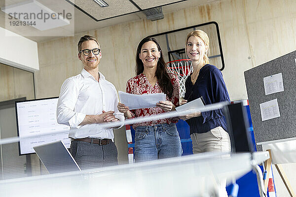 Glückliche Geschäftsleute stehen mit Dokumenten im modernen Büro