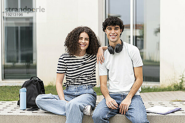 Glückliche Studenten sitzen auf einer Betonbank vor dem Gebäude