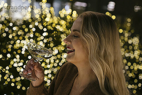 Glückliche Frau hält Champagnerglas neben Weihnachtsbeleuchtung