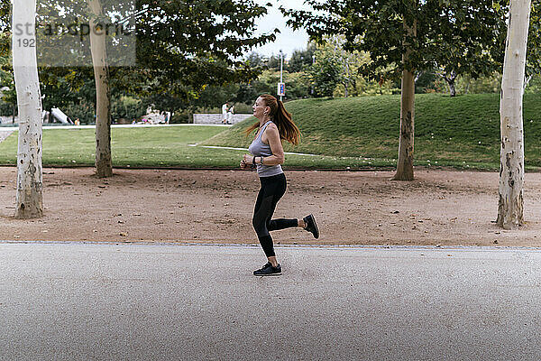 Rothaarige Frau joggt auf Fußweg im Park