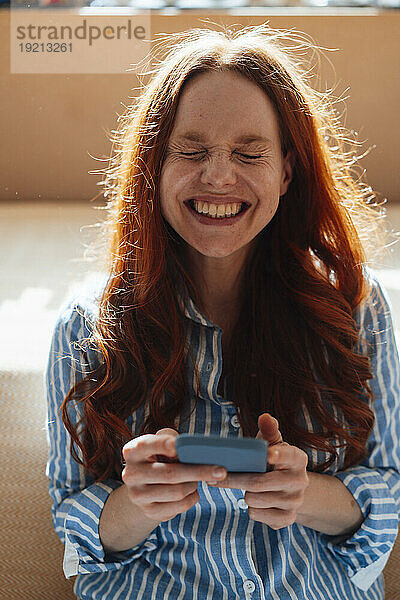 Cheerful woman with smart phone sitting at home