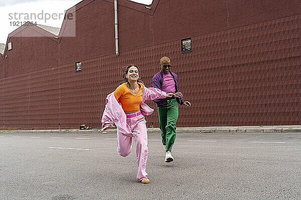 Fröhliche Frau rennt und hat Spaß mit einer Freundin vor dem Gebäude