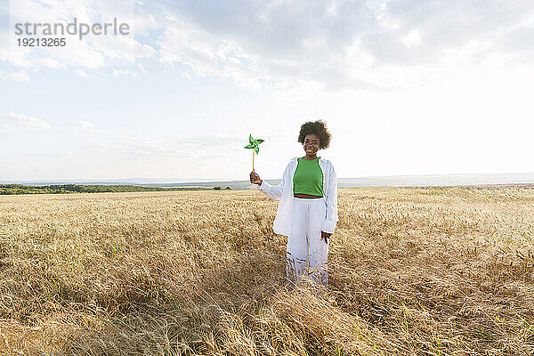 Smiling woman holding pinwheel toy standing amidst plants in field