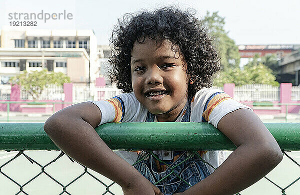 Happy boy leaning on fence at sports court