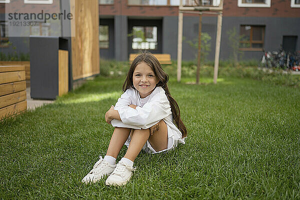 Lächelndes Mädchen sitzt auf Gras im Hinterhof