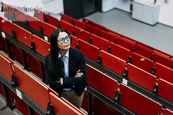 Businesswoman with arms crossed standing amidst seats at convention center