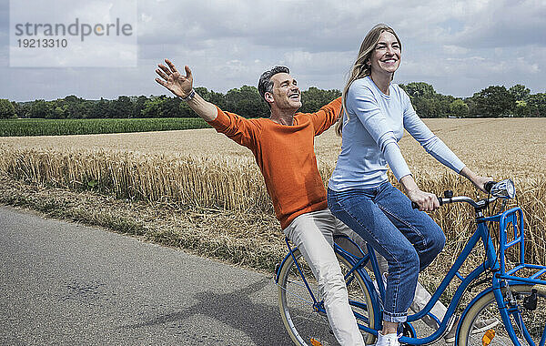 Reifer Mann genießt Fahrradtour mit Frau in der Nähe des Feldes