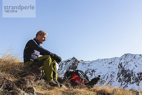 Contemplative man sitting with backpack on mountain in winter