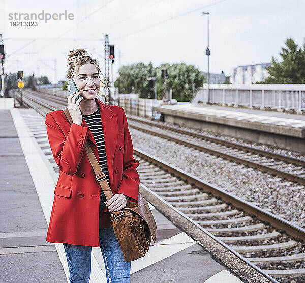 Glückliche Frau  die am Bahnhof mit dem Smartphone spricht