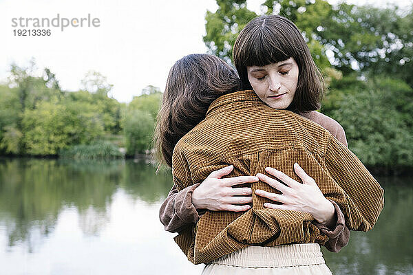 Liebevolle Zwillingsschwestern umarmen sich in der Nähe des Sees