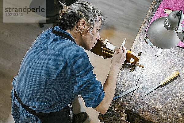 Instrumentenbauer arbeitet am Schreibtisch in der Werkstatt an der Geige
